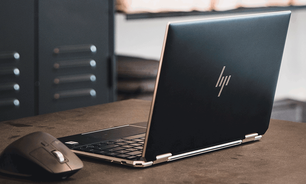 An HP laptop sits open a desk with a mouse beside it.